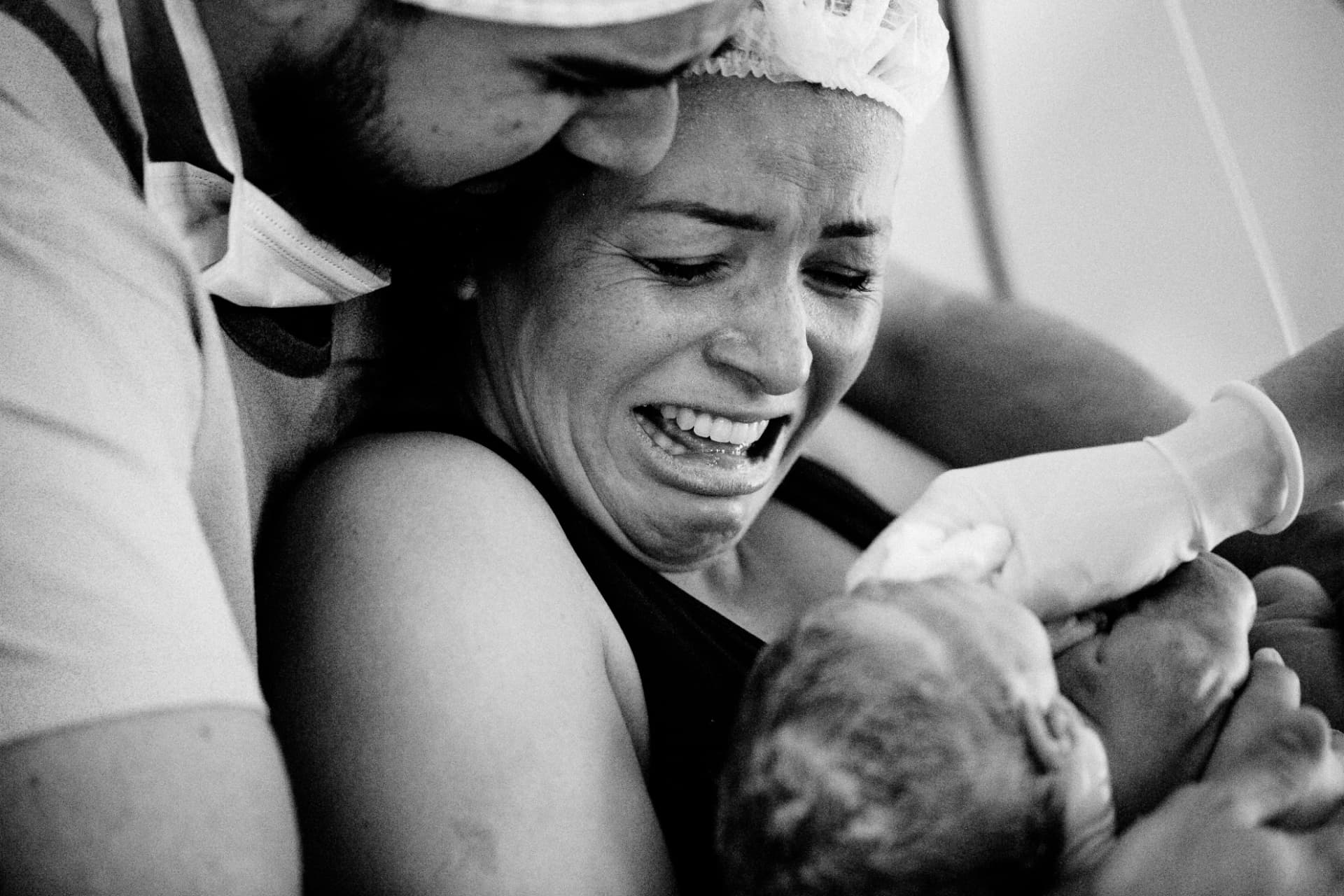 Mãe emocionada recebendo o bebê no colo, com o pai ao lado