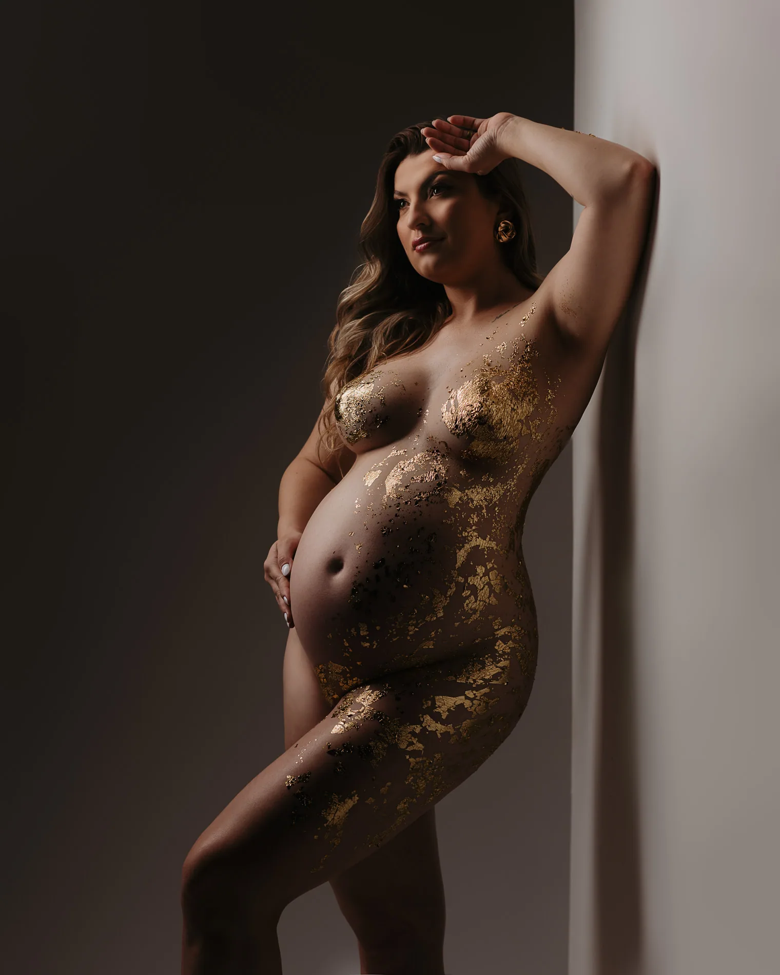 Gestante com pintura dourada no corpo, retrato em luz lateral