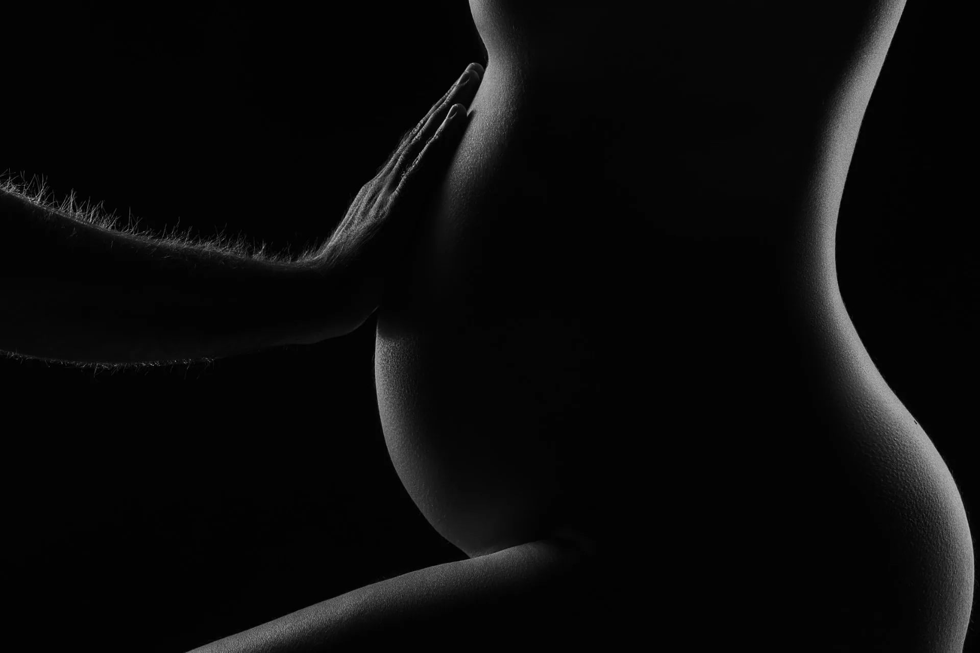Detalhe em preto e branco das mãos do casal sobre a barriga