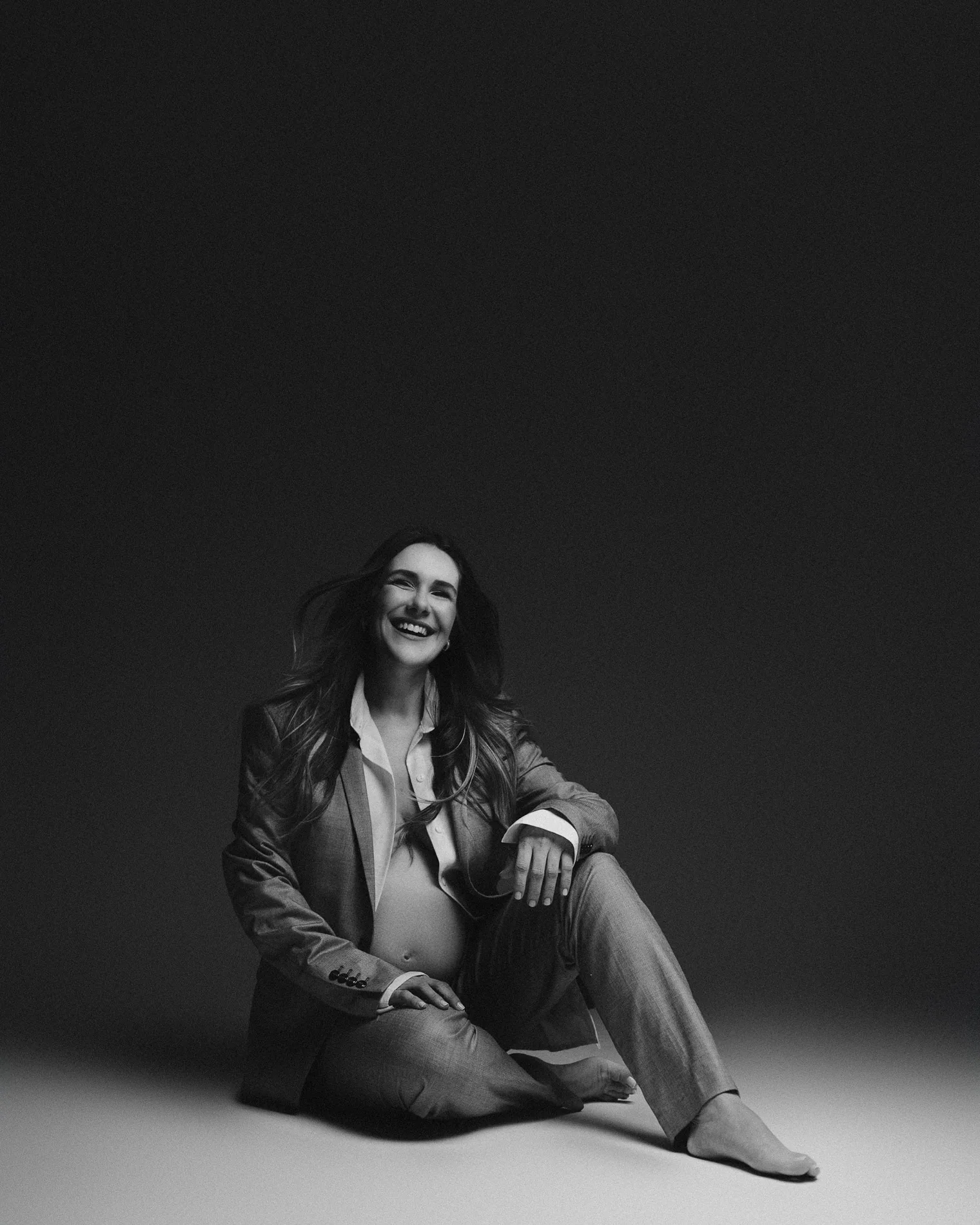 Gestante sorrindo com terno em preto e branco, sentada no chão