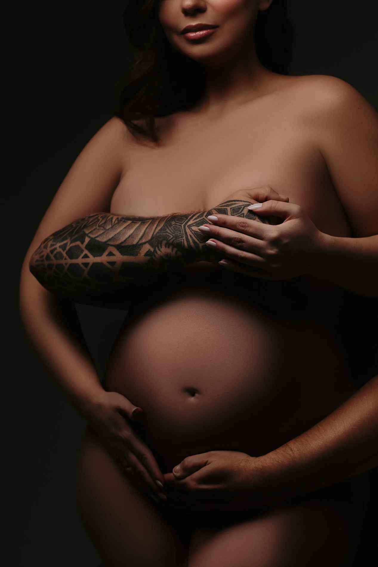 Abraço do casal sobre a barriga da gestante em luz baixa