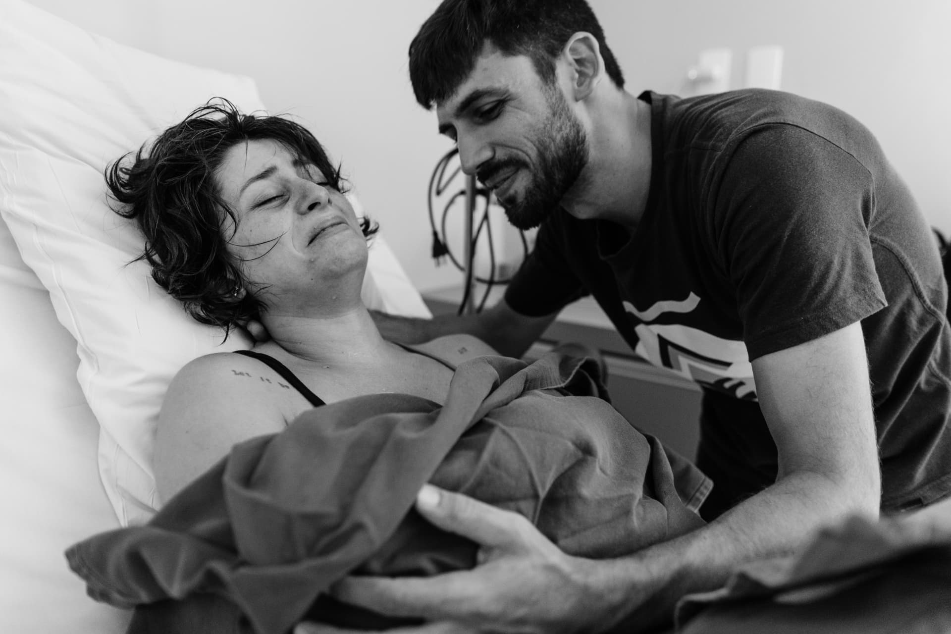 Casal no leito da maternidade com o bebê recém-nascido nos braços