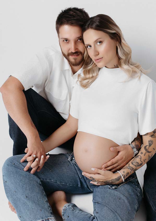 Casal em ensaio de gestante, abraço com as mãos na barriga em cenário minimalista