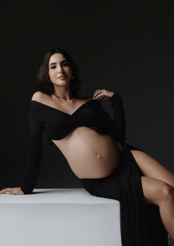 Gestante de perfil em estúdio, mãos sobre a barriga, luz lateral suave em fundo neutro