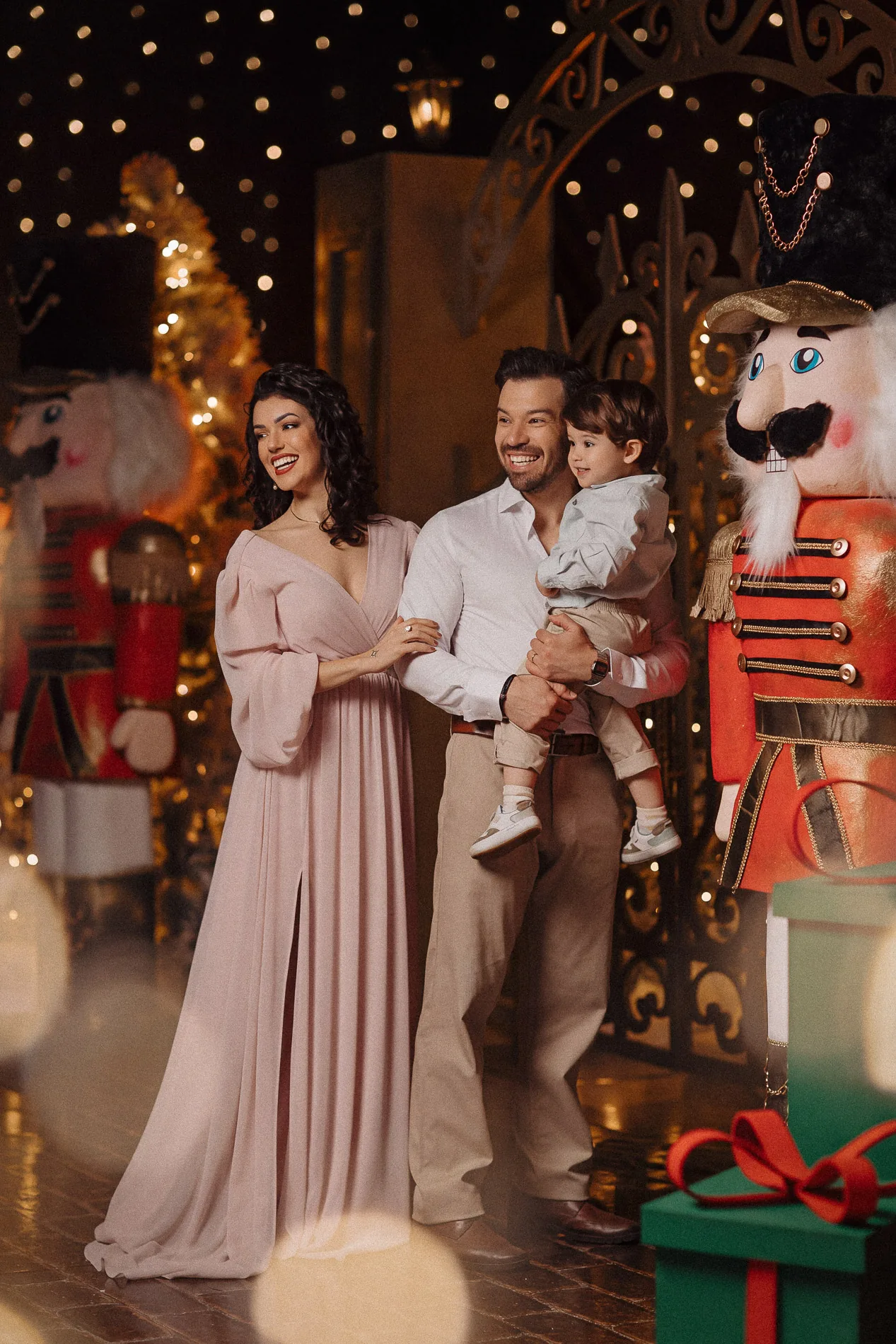 Casal com a criança no colo diante do portão iluminado de Natal.