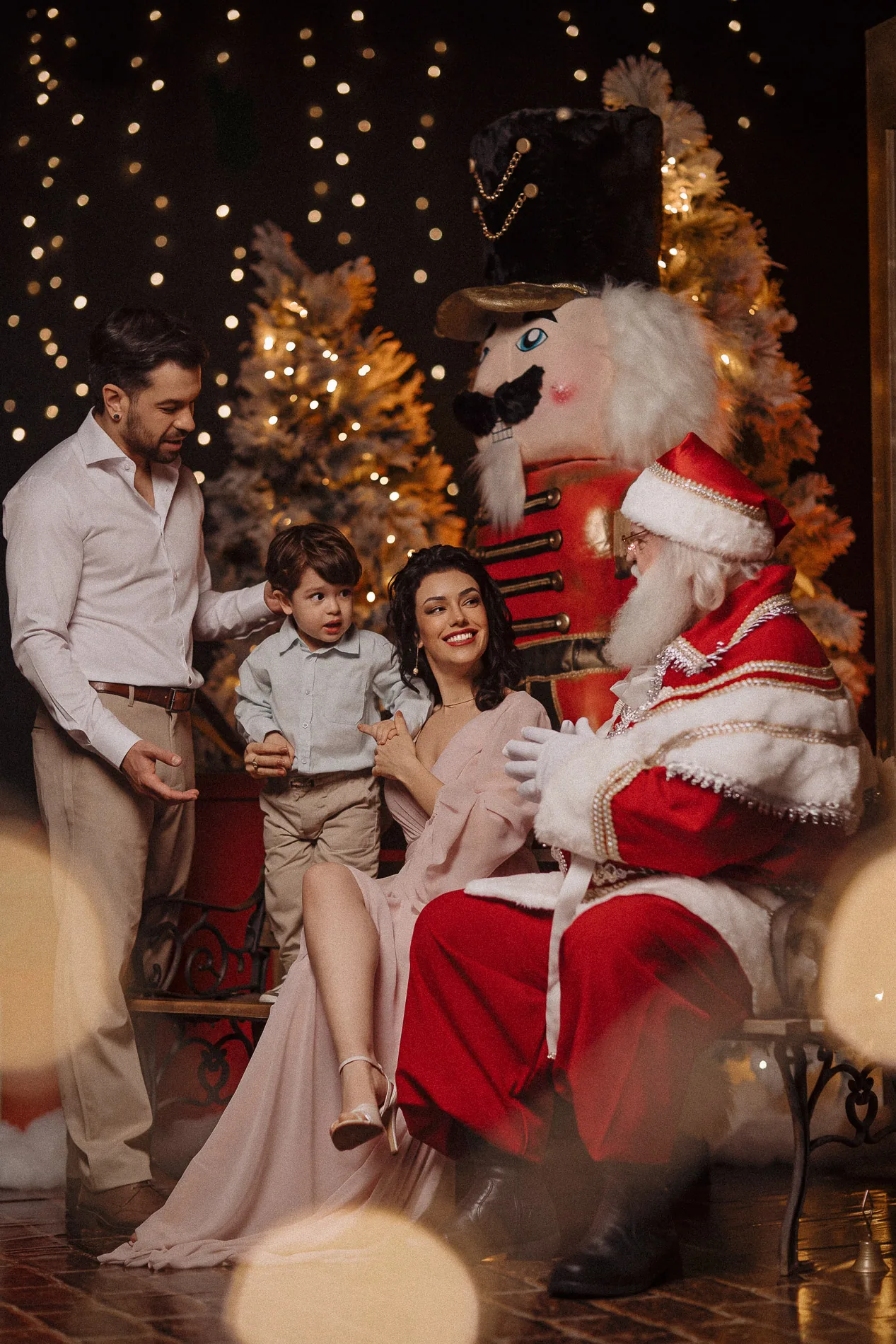 Família sentada com Papai Noel no cenário iluminado de Natal.